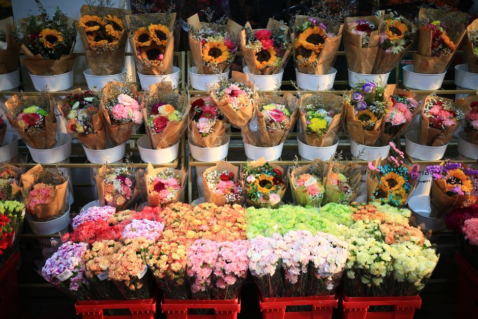 A vibrant display of fresh flower bouquets arranged on shelves at flowersleabridge.co.uk, featuring a variety of blooms including sunflowers, roses, carnations, and chrysanthemums in shades of yellow,