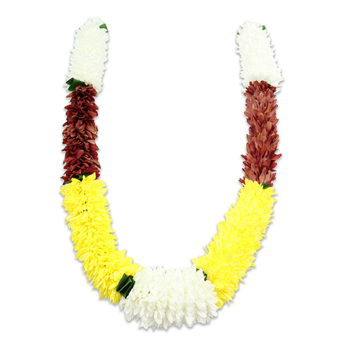 A vividly coloured U-shaped garland, photographed on a pure white surface so every petal and shadow reads clearly, reveals the thoughtful artistry of traditional mala-making. Densely formed from synthetic fabric petals, the garland's texture is sumptuous and even-each section composed of thousands of tiny, carefully arranged petals that create a soft, cushion-like appearance. From the top of each arm, a generous segment of pure white blooms-suggestive of chrysanthemums or jasmine-inspired forms-provides a clean, serene introduction. Below this is a compact, richly hued maroon band, the reddish-brown tones adding depth and a sense of reverent warmth. The design then flows into the most expansive portion: a long, bright yellow section that arcs through the lower U, echoing marigold's sunny cheer and filling the visual field with generous colour. At the lowest point the two yellow arms meet in a fuller cluster of white blossoms, slightly broader than the upper white segments and subtly separated by small dark green leaf accents that punctuate the colour transitions. As a florist at Flowers Lea Bridge with years of local experience around Lea Bridge Road and the nearby station, I appreciate how this artificial garland combines durability with ceremonial beauty-ideal for Hindu puja, temple offerings, Diwali decorations, or as a respectful tribute at weddings. The palette-white for purity, yellow for prosperity, maroon for devotion-carries cultural resonance while the meticulous construction promises enduring colour and form.