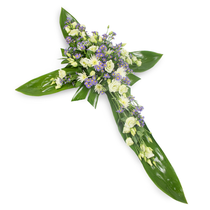 This heartfelt cross, photographed slightly from above on a stark white plane, combines classical form with a natural, garden-like softness. The foundation is composed of broad, glossy tropical leaves-Ti-style foliage-each placed with intention so the veins and reflective surfaces describe the cross's arms and centre with clean geometry. Nestled into that verdant base is a dense, tender arrangement of pale florals: creamy ivory and pure white lisianthus with their layered, ruffled petals and soft closed buds, arranged to create a plush focal point at the intersection and extending outward along each arm. Intermingled are small, white daisy-like chrysanthemums whose compact shapes add luminosity and a tactile contrast to the lisianthus. Delicate sprays of lavender-toned limonium or tiny asters introduce a cool, restrained colour accent that deepens the composition without overwhelming it, while finer green filler foliage slips through the clusters to give a sense of natural growth and gentle movement. The overall light is soft and balanced, revealing the subtle tactile differences-the waxy sheen of the leaves against the velvety, feathery bloom surfaces-while keeping the mood serene and dignified. There is a faint, green, herbal scent and a sense of calm stillness to the arrangement, making it suitable for religious services, memorials, and graveside remembrances. As crafted for contemplative moments, this cross conveys respect, consolation and the quiet hope of continuity in a respectful, understated manner.