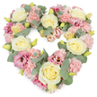 A densely flowered, heart-shaped wreath fills the frame, the pastel blooms glowing softly against a bright white background. The heart is formed from a careful mingling of cream and pale yellow roses, pastel pink carnations, deeper pink lisianthus, and cool eucalyptus foliage, all placed so closely together that the flowers appear to touch and support one another. The roses, with their rounded, layered petals, sit proudly across the design, giving structure and a serene elegance. Around them, the ruffled carnations add a billowing, cushion-like texture, their gentle pink tones evoking tenderness and affection. Scattered among these are lisianthus blooms in richer shades of mauve and magenta-pink, their open, slightly curled petals adding depth and a hint of contemporary style to this classic tribute. Small yellow-green buds are visible at intervals, bringing a sense of freshness and vitality, as though the wreath has just been completed and is ready to be taken to a service. Silvery eucalyptus leaves weave between the flowers, their round shapes and muted green colour tracing the outline of the heart and echoing the calm greenery found in nearby Millfields Park and along the Lea Bridge waterways. The overall look is lush yet gentle, with a soothing blend of pink, cream, and green tones that communicate love, remembrance, and quiet support. This heart-shaped arrangement feels particularly suited to funerals, memorials, or graveside tributes in Lea Bridge, offering families a dignified and beautiful way to say a final, heartfelt farewell.