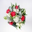 A hand-tied bouquet viewed from above, filled with crimson roses, pink-red carnations, and soft white daisies, looks as if someone has gathered a perfect armful of early morning light from a Lea Bridge garden. The roses sit proudly at the heart of the arrangement, their velvety petals spiralling in deep, confident reds that suggest romance, congratulations, or a warm welcome home. Around them, ruffled carnations in matching tones feel almost feathery, their layered edges catching the light and adding playful movement to the design. Clusters of tiny white chrysanthemum-style daisies and airy gypsophila glow like scattered stars, softening the intensity of the reds and giving the bouquet a gentle, cloudlike halo. The foliage is a composed mix of eucalyptus and glossy tropical greens, their cool blue-green and deep forest tones grounding the brighter colours. Each leaf has a distinct shape and texture: thin eucalyptus ovals with a whisper of silver, broader tropical fronds that frame and support the blooms from beneath. The flowers appear freshly cut, petals crisp and hydrated, as though they have just arrived from a nearby market stall off Lea Bridge Road. The mood of the bouquet is joyful yet calm, perfect for setting on a kitchen table flooded with daylight, for celebrating a birthday in a flat overlooking Millfields Park, or for surprising someone after a long day's commute through East London. Every element feels thoughtfully chosen and placed, reflecting the steady hands and trained eye of a local florist who understands how colour, scent, and form come together to create a moment of shared happiness in the heart of Lea Bridge.