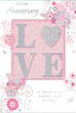 In this image, a beautifully designed anniversary card rests against a plain backdrop, allowing its romantic details to shine. The focal point is the word LOVE, arranged in raised letters so softly glittered that they feel like they have been dusted with silver mist. The letter O is subtly transformed into a shimmering silver heart, slightly more textured than the other letters, drawing the eye to the very centre of the design like a cherished keepsake exchanged year after year in a Lea Bridge home. Surrounding this word, delicate blossoms in blush pink and soft mauve unfurl with a watercolour-like softness, their edges gently blurred while their stems and vines are drawn in more defined, flowing lines. These flourishes give the impression of an English spring garden, similar to the gentle plantings you might notice along quiet streets off Lea Bridge Road or beside the towpaths near the River Lea. Tiny butterflies, swirling tendrils, and scattered petals appear almost to move across the front of the card, adding a graceful sense of motion and whimsy. Above and below the central motif, phrases such as On Our Anniversary and I love you today and always are written in a refined, script-like font, the lettering slim and slightly curved, radiating warmth without overpowering the artwork. The colour story is soft pastel pinks balanced with silvery greys and pearl whites, creating a mood of treasured intimacy. Altogether, the card feels like a tender paper companion to a fresh bouquet, the sort of keepsake lovingly chosen to mark a shared journey in Lea Bridge.